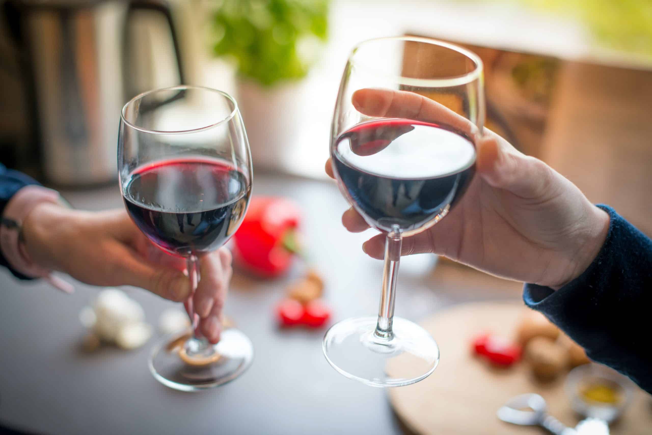 Twee mensen proosten met een glas rode wijn.