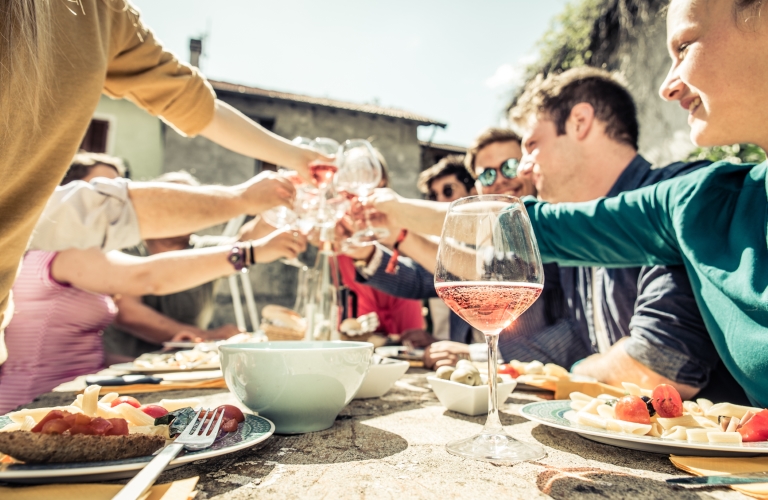 Wijnmarkt 2023 - Groep mensen proost samen aan een buitentafel met roséwijn en eten op een zonnige dag.