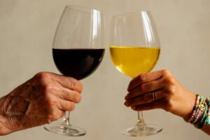 Links een oude mannenhand met een glas rode wijn en rechts een jonge vrouwenhand met een glas witte wijn