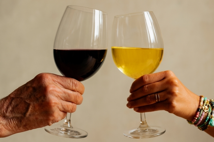 Links een oude mannenhand met een glas rode wijn en rechts een jonge vrouwenhand met een glas witte wijn