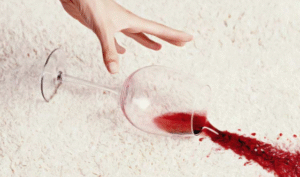 Omgevallen glas rode wijn op tapijt, met een hand die het glas gaat oprapen