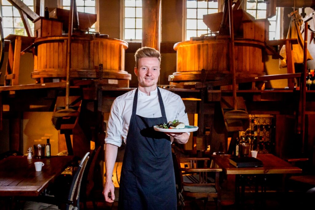 Ramon Klaaasen staat in restaurant de Watermolen voor het antieke nog werkende waterrad