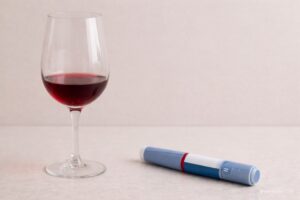 Een halfvol glas rode wijn en een Ozempic spuit